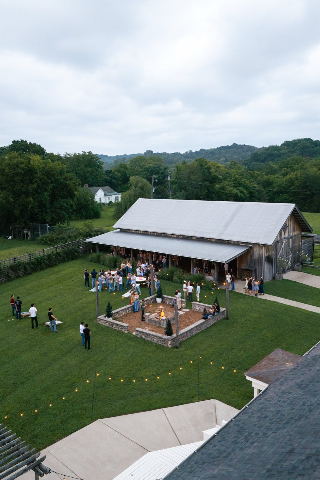 Aerial view of the barn venue with fire pit, lawn games, and crowd at dusk
